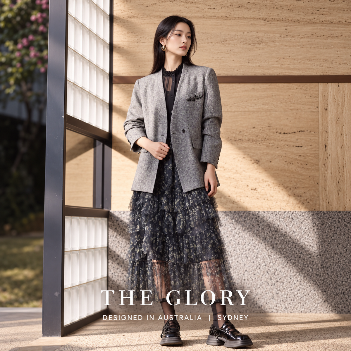 Model wearing a grey V-neck blazer over a black blouse and patterned skirt.