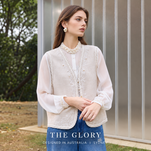 Model wearing a pale apricot embroidered vest over a white blouse with blue jeans.